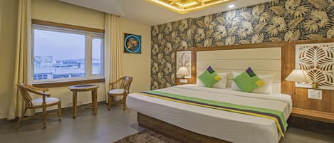 Habitación de hotel con una cama grande, dos sillas, una mesita y vistas a la ciudad, además de un papel tapiz tropical.