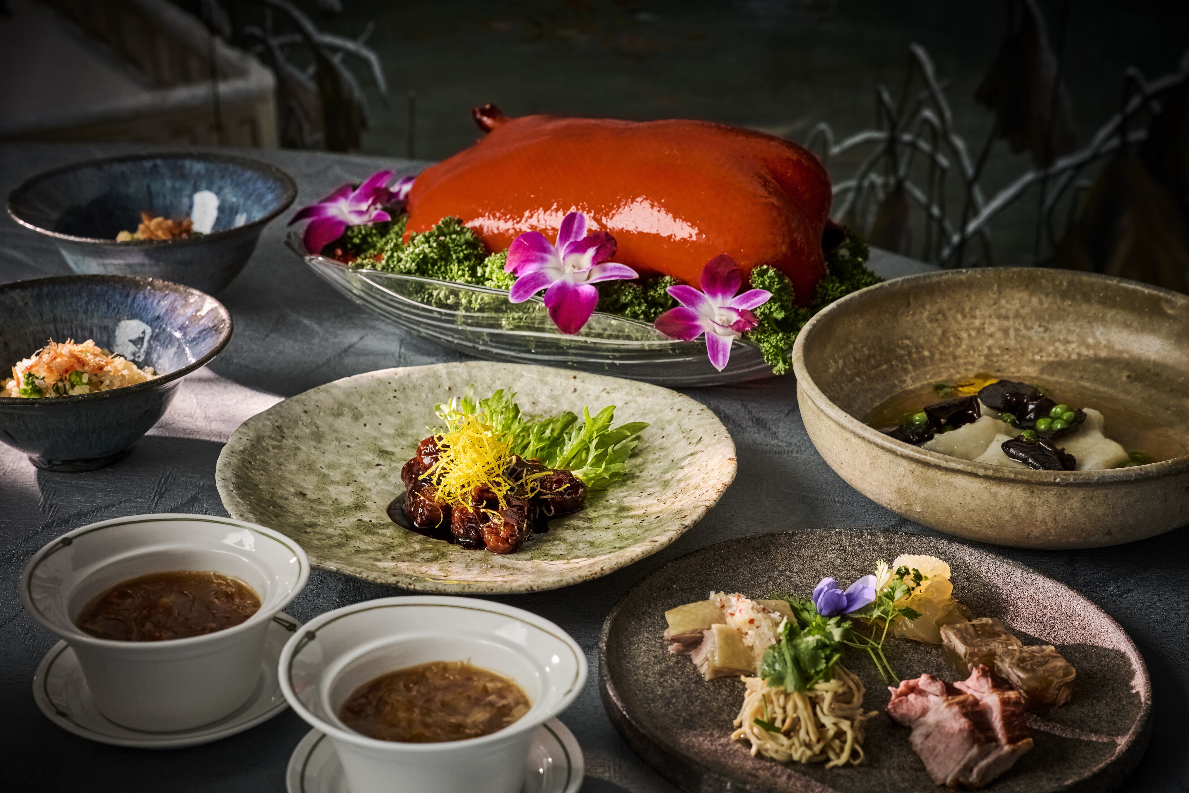 A variety of dishes including a roasted pig, bowls of soup, and plates with vegetables and meat.