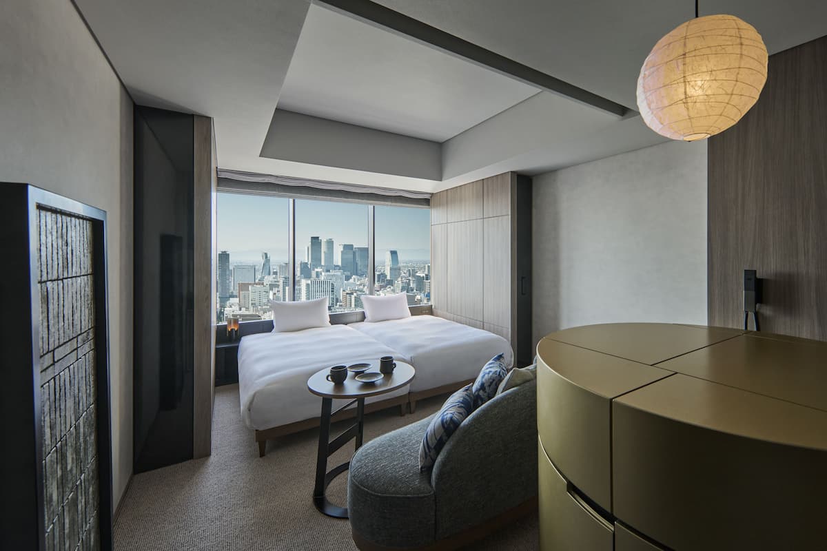 A modern hotel room with a large bed, a seating area, and a view of the city skyline.