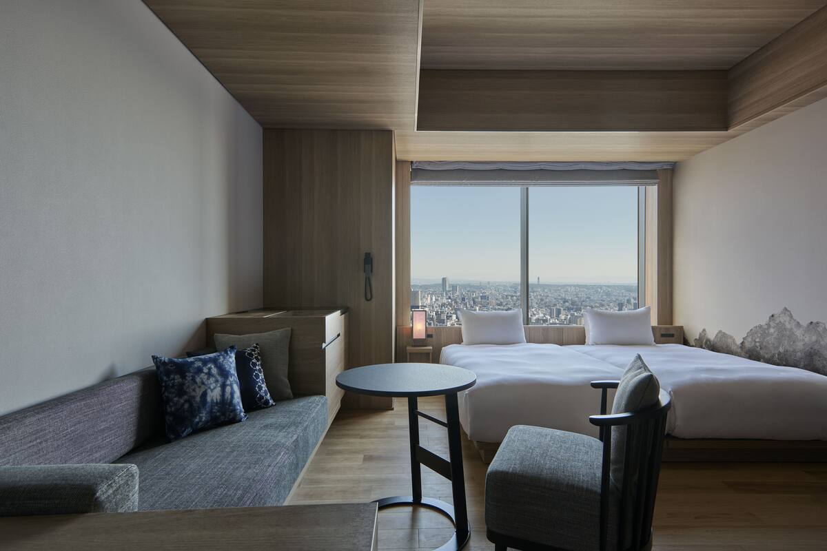 A modern hotel room with a large bed, a sofa, a small table, and a view of the city.