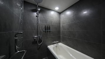 A modern bathroom with a bathtub, a shower with a handheld showerhead, and a glass shelf with toiletries.