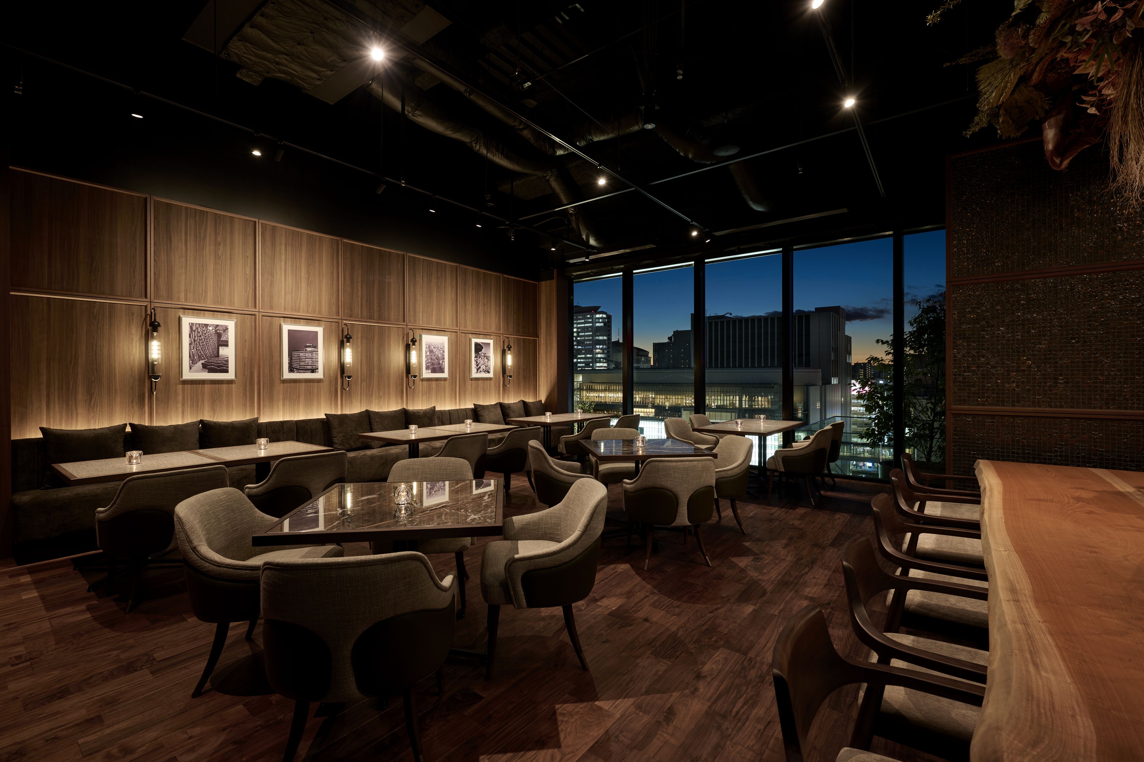 En modern restaurang med träpanel, flera sittområden och stora fönster med utsikt över staden.