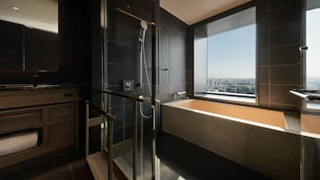 A modern bathroom with a glass-enclosed shower, a large bathtub, and a city view through a large window.