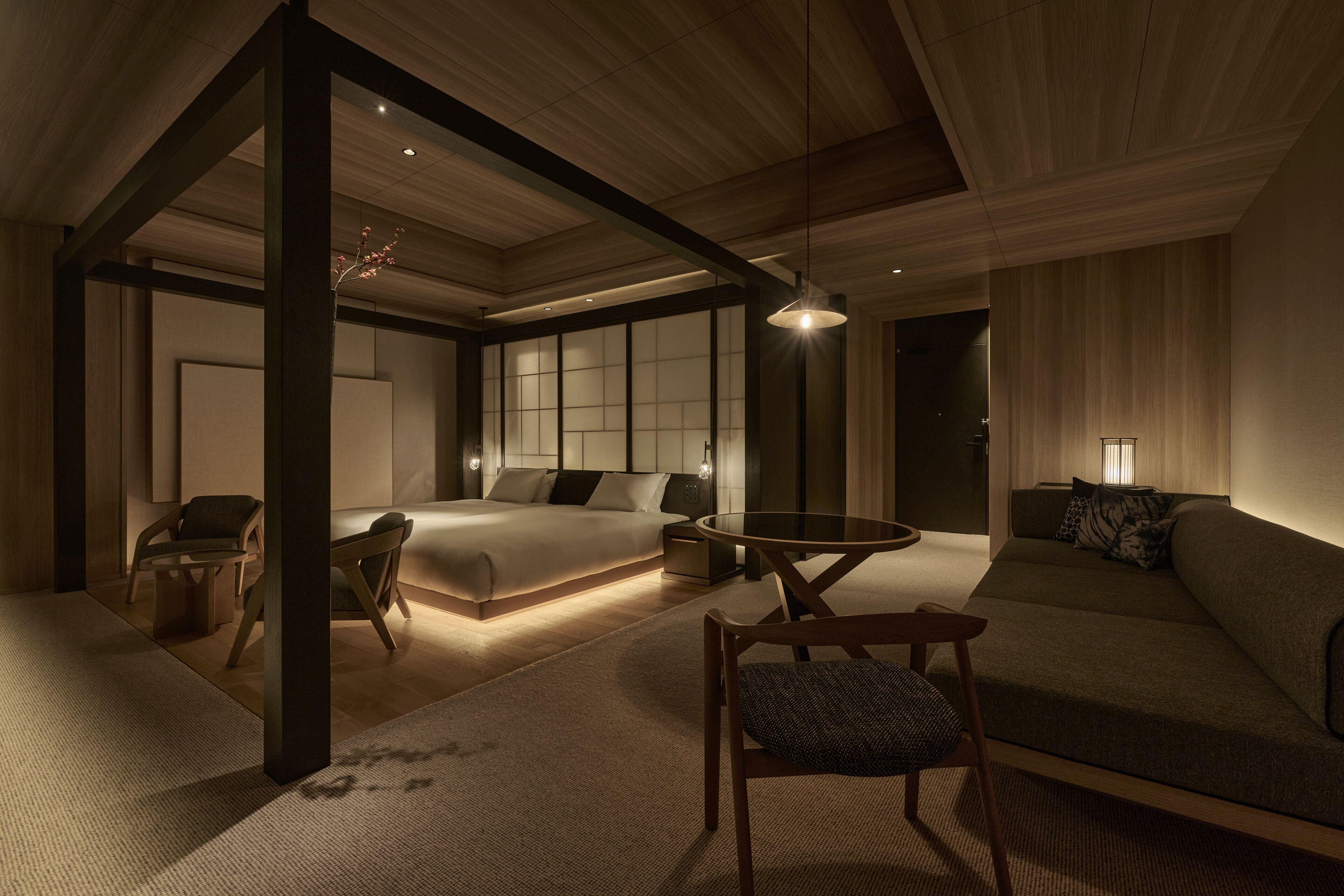 A modern bedroom with a large bed, a sofa, a dining table, and a chair.