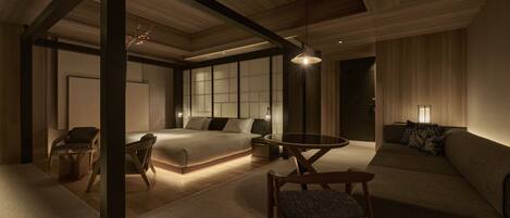 A modern bedroom with a large bed, a sofa, a dining table, and a chair.
