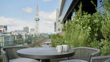 Una mesa redonda con dos tazas blancas en un balcón con vista a una ciudad, con edificios modernos y una torre.