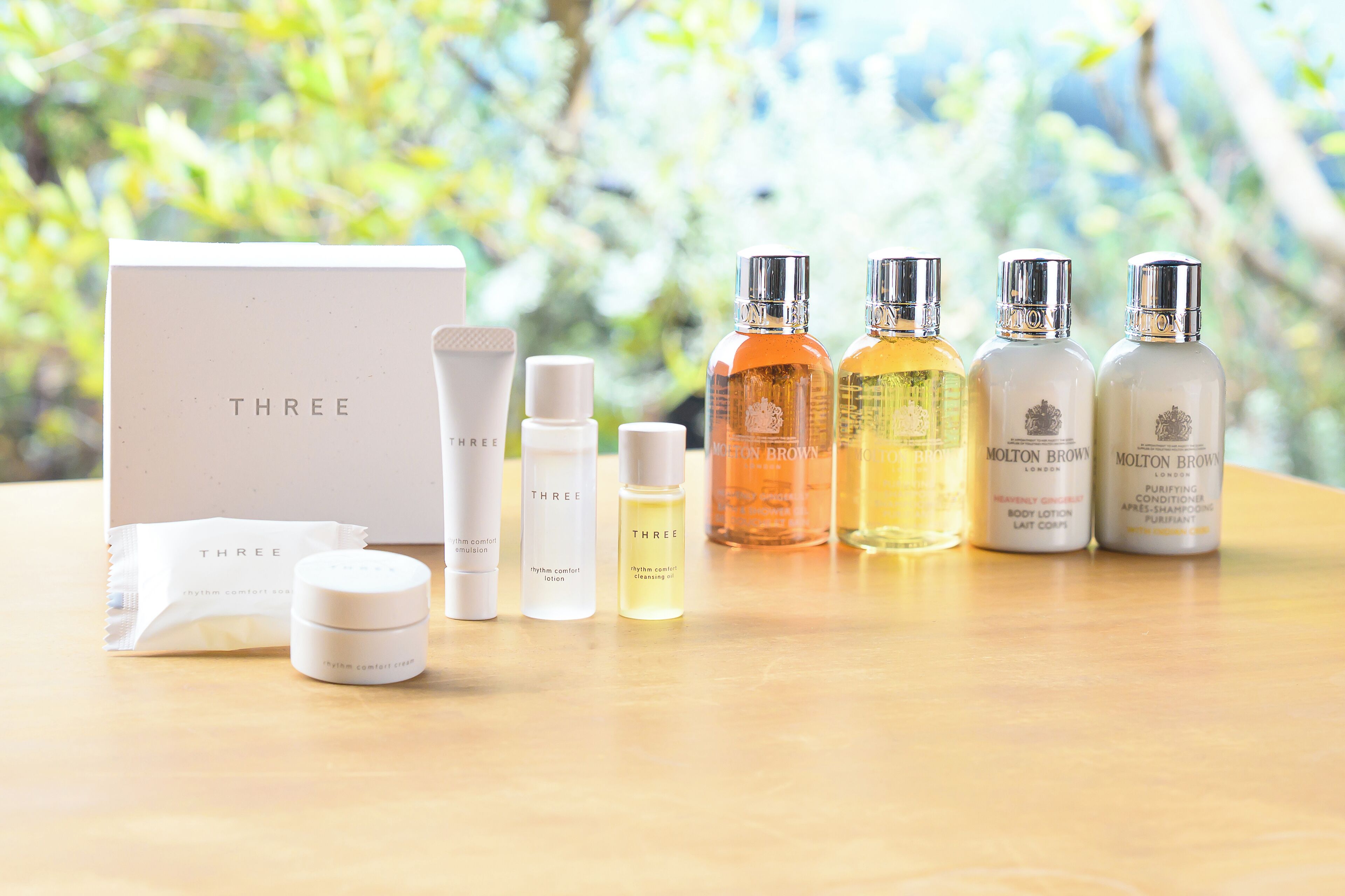 A skincare set with bottles and a box labeled "THREE" on a wooden surface with a blurred green background.