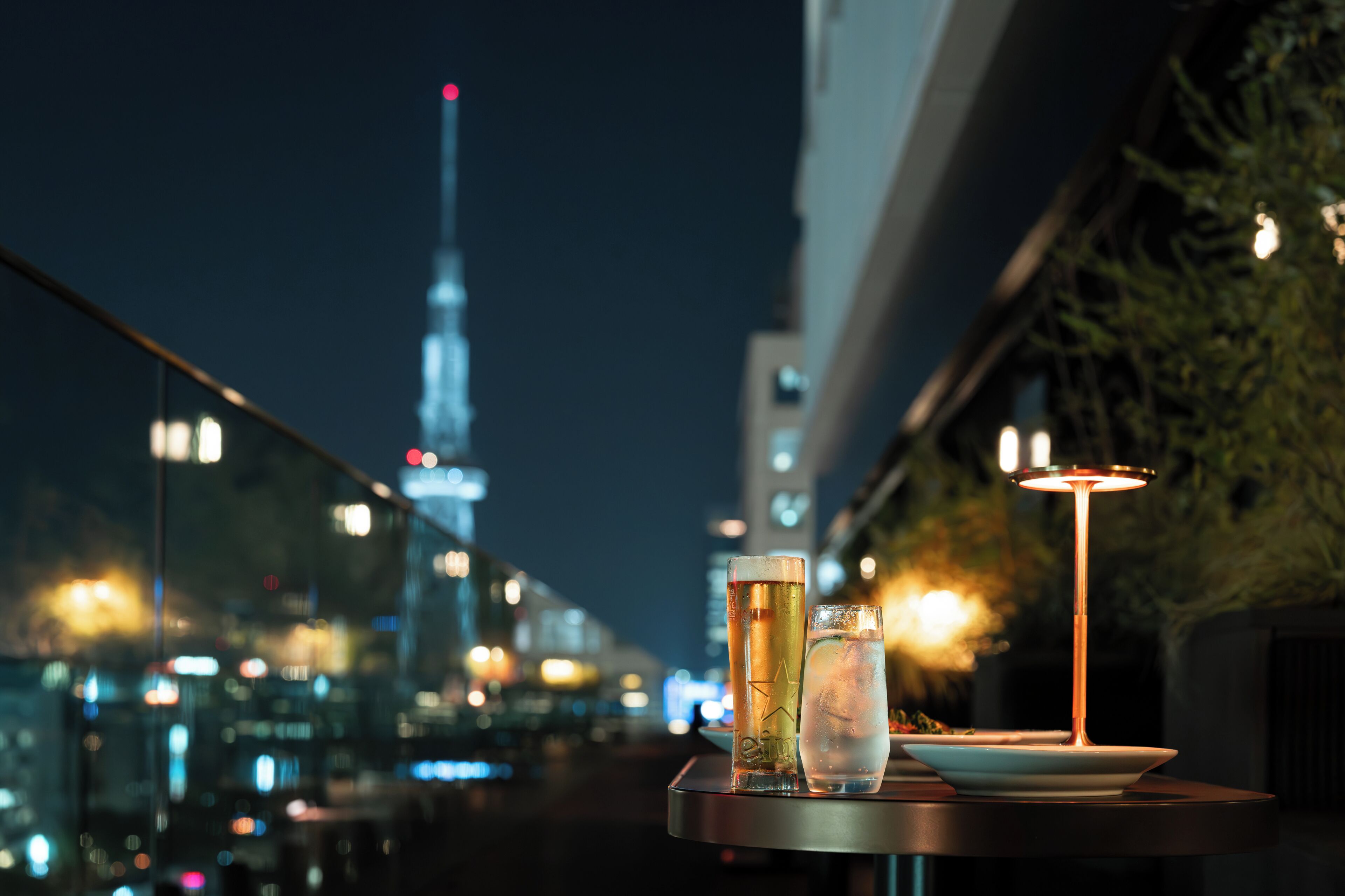 Una mesa con bebidas y una lámpara, con vistas a un paisaje urbano que destaca una torre imponente.