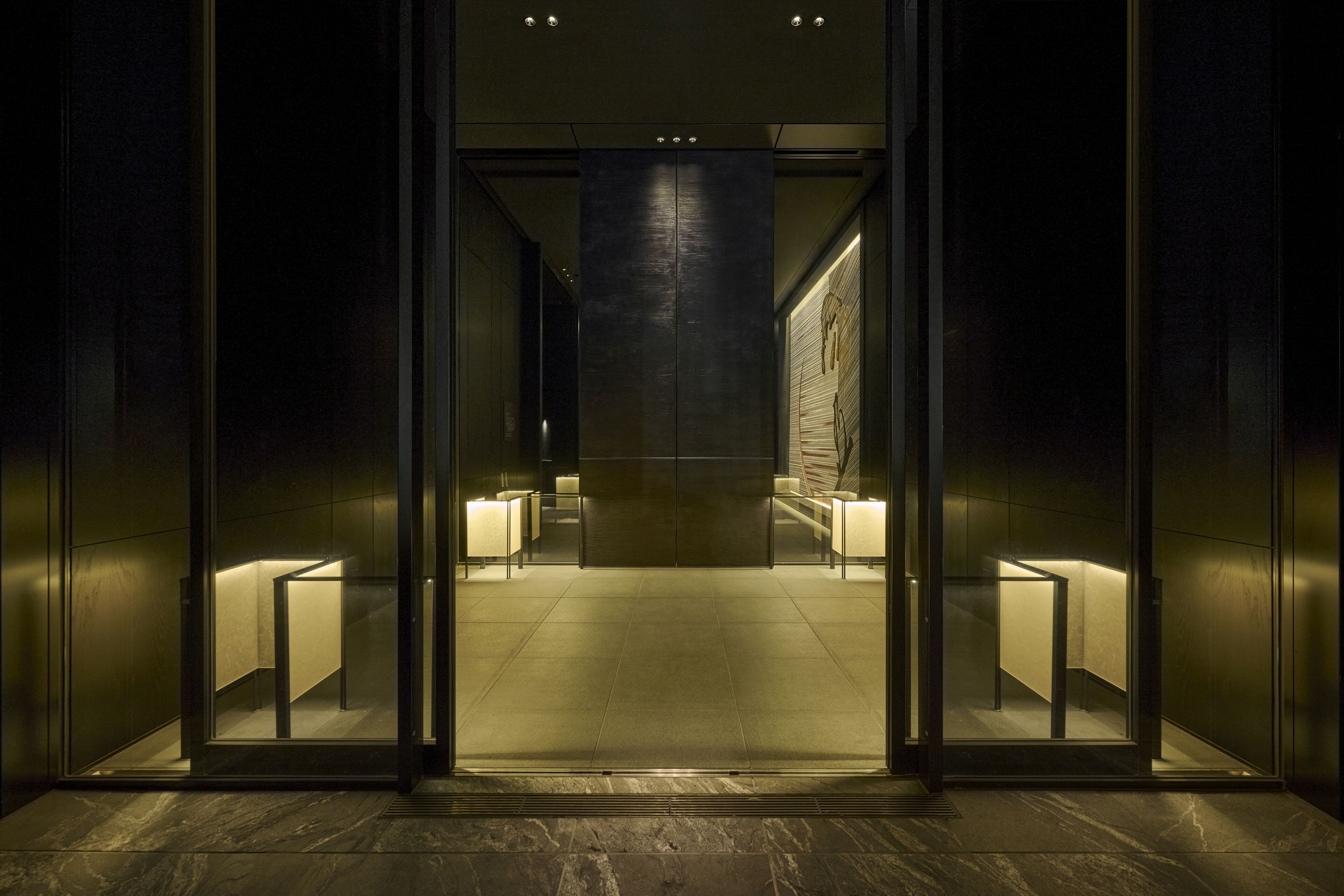A modern elevator with glass doors, a dark interior, and illuminated walls.