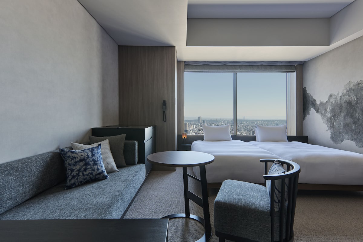 A modern hotel room with a large bed, a sofa, a small table, and a view of the city.