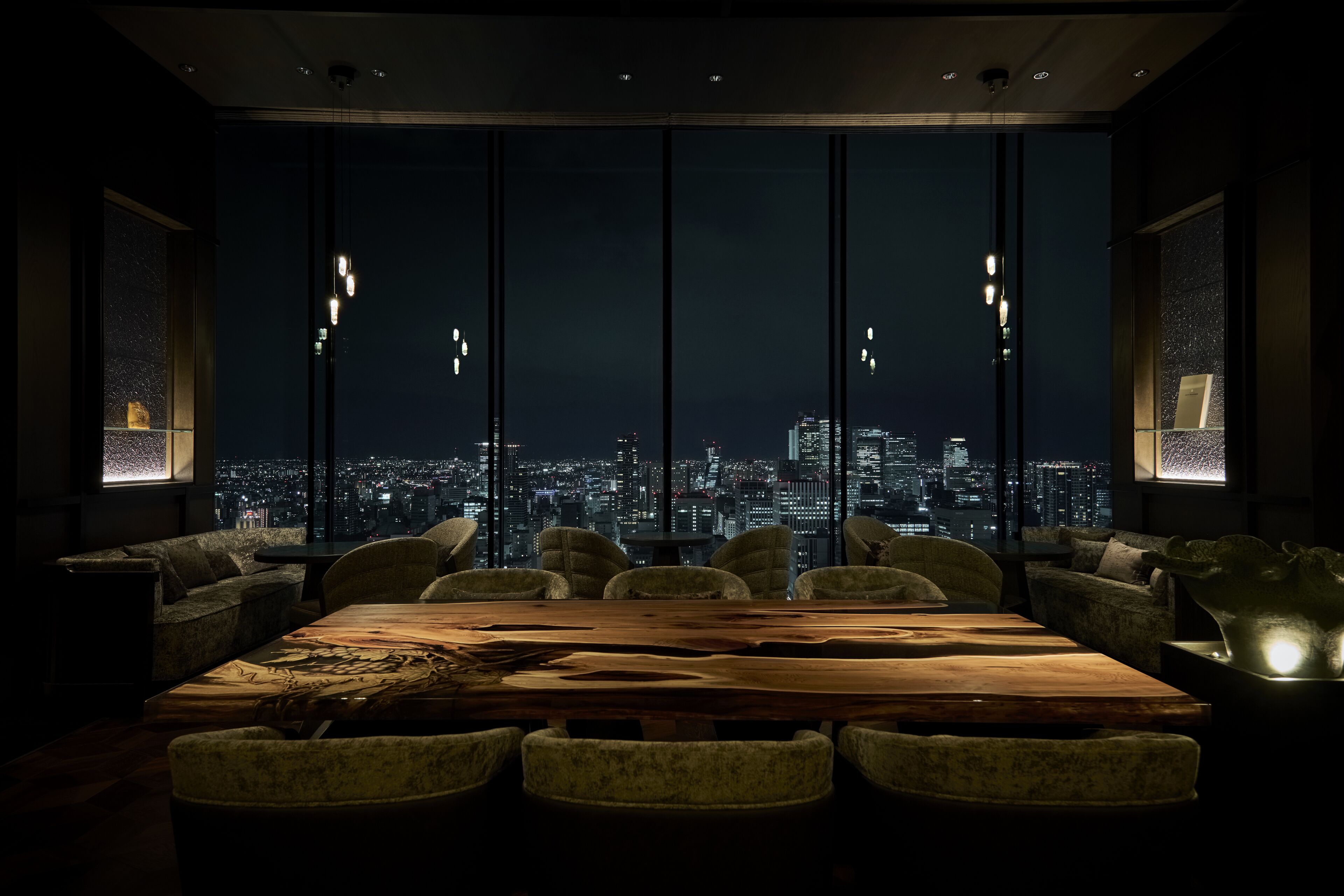 Un comedor moderno con una amplia mesa de madera y asientos cómodos, con vistas a la ciudad iluminada de noche.