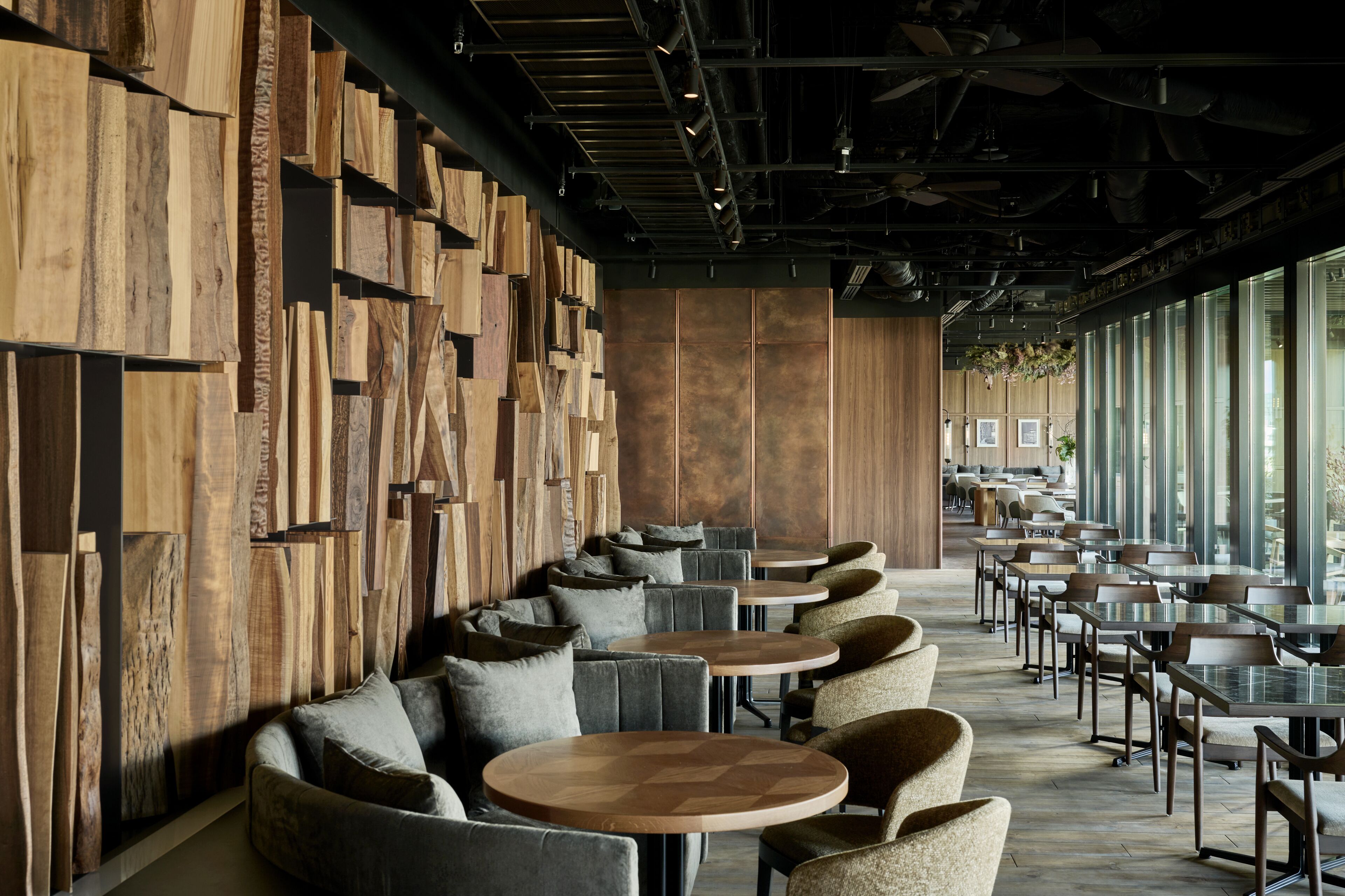 A modern restaurant with wooden wall panels, round tables, and cushioned seating.