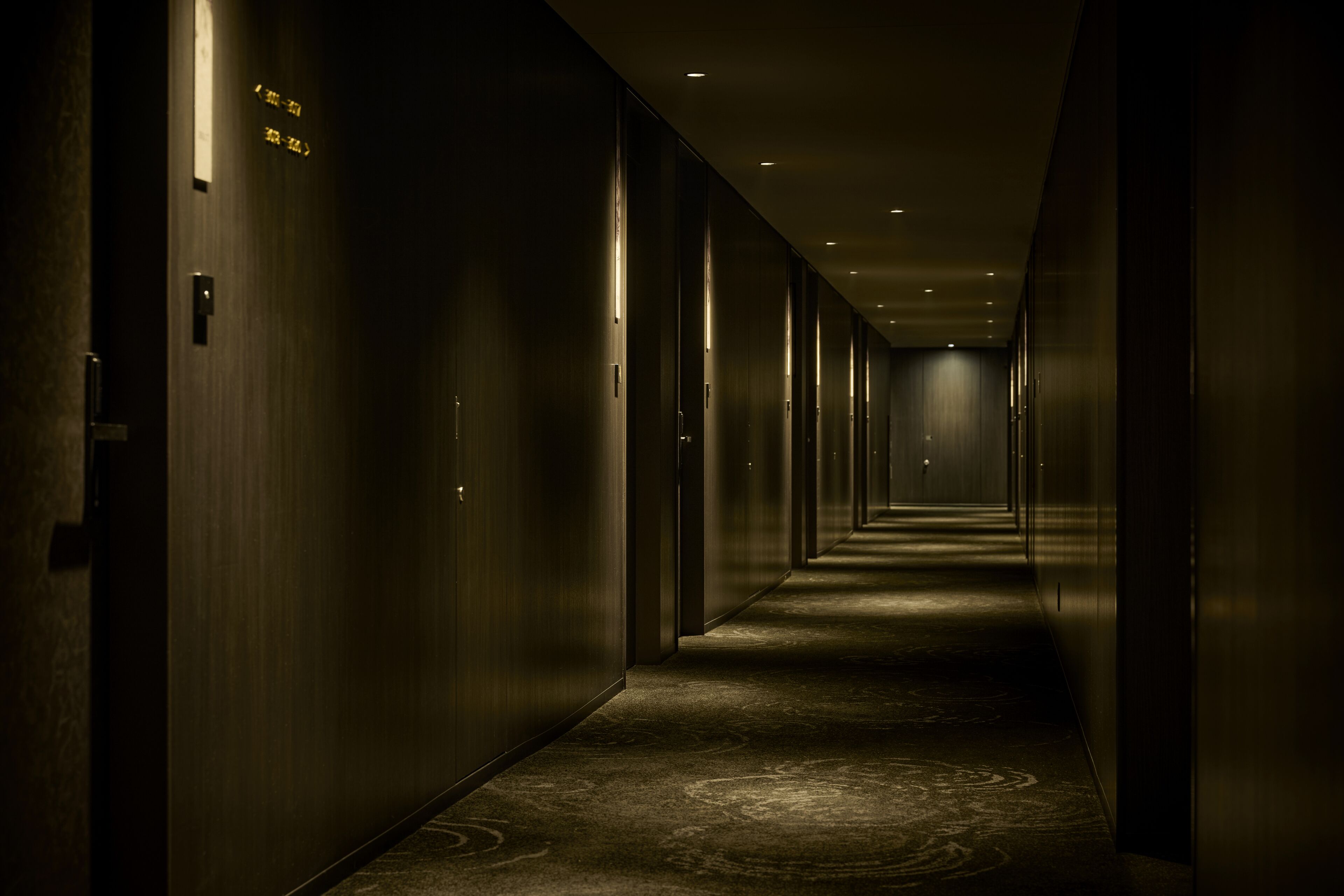 A long, narrow hallway with doors on both sides, illuminated by overhead lights.