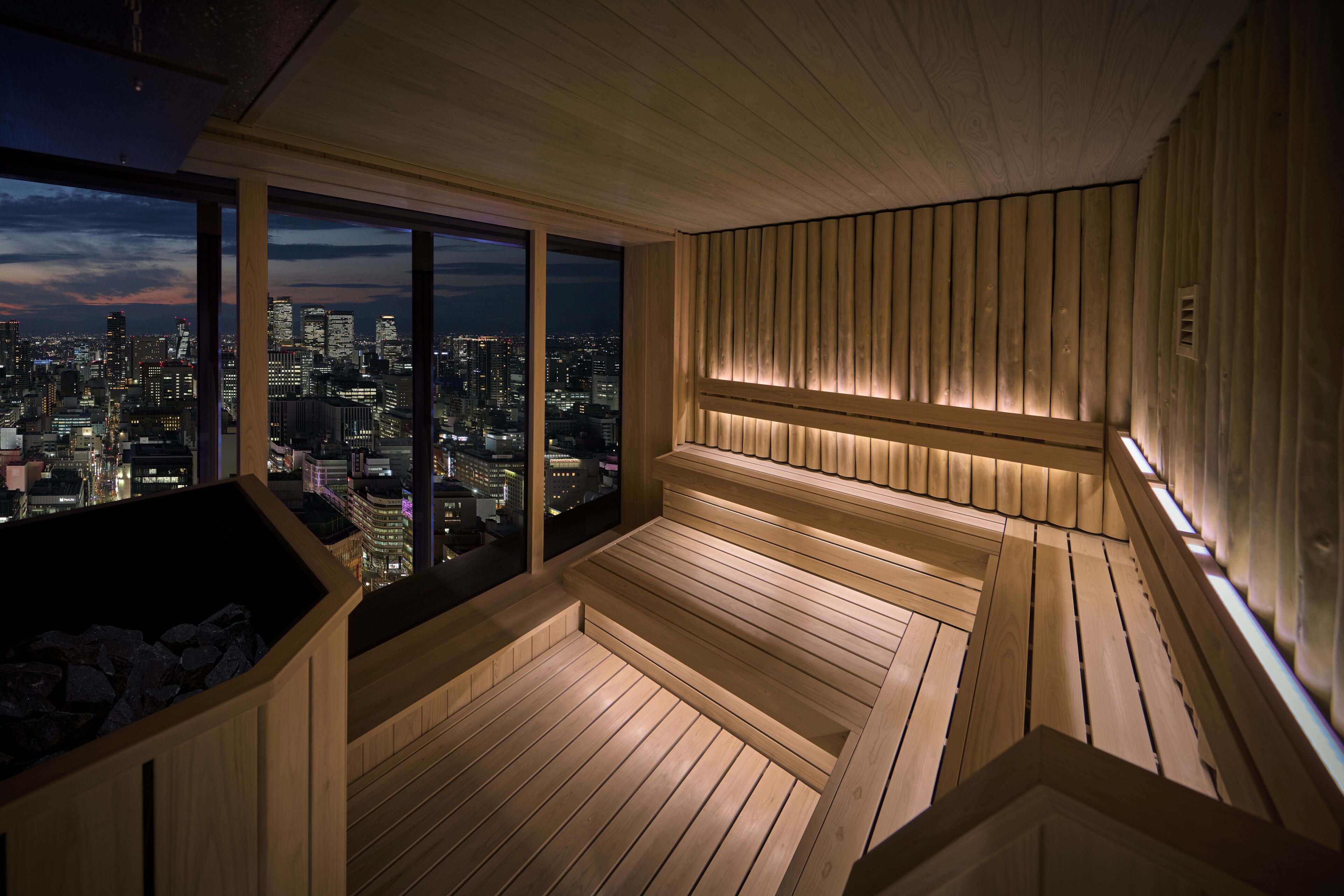 A wooden sauna with a city view, featuring a bench and a heated floor.