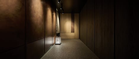 Un pasillo estrecho con paneles de madera y suelo alfombrado, que conduce a una habitación con pared texturizada y una pequeña caja en el suelo.