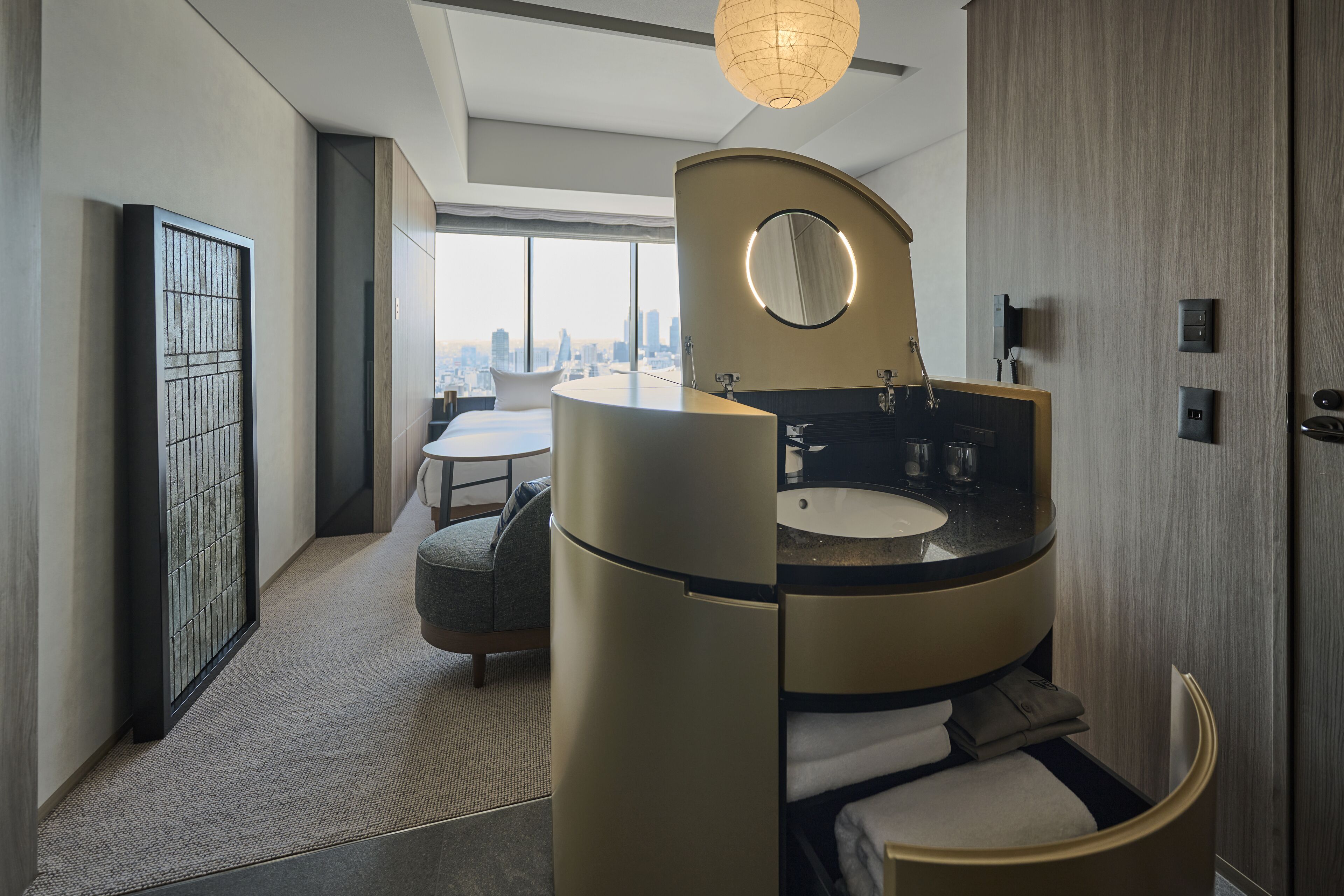 A modern bathroom with a curved sink, a round mirror, and a view of the city skyline.