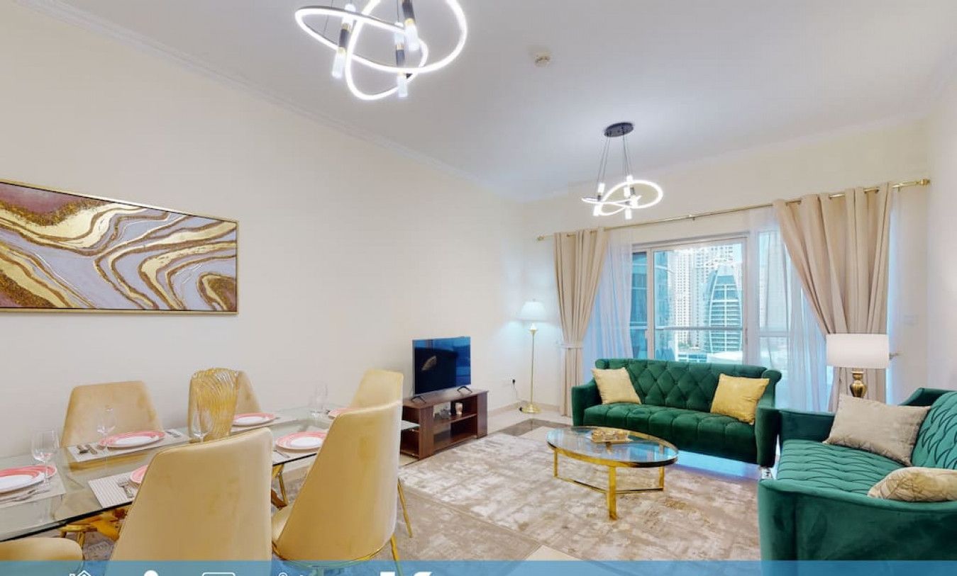 A spacious living room with a green sofa, a dining area with chairs, a TV, and a painting on the wall. There are curtains and a lamp.