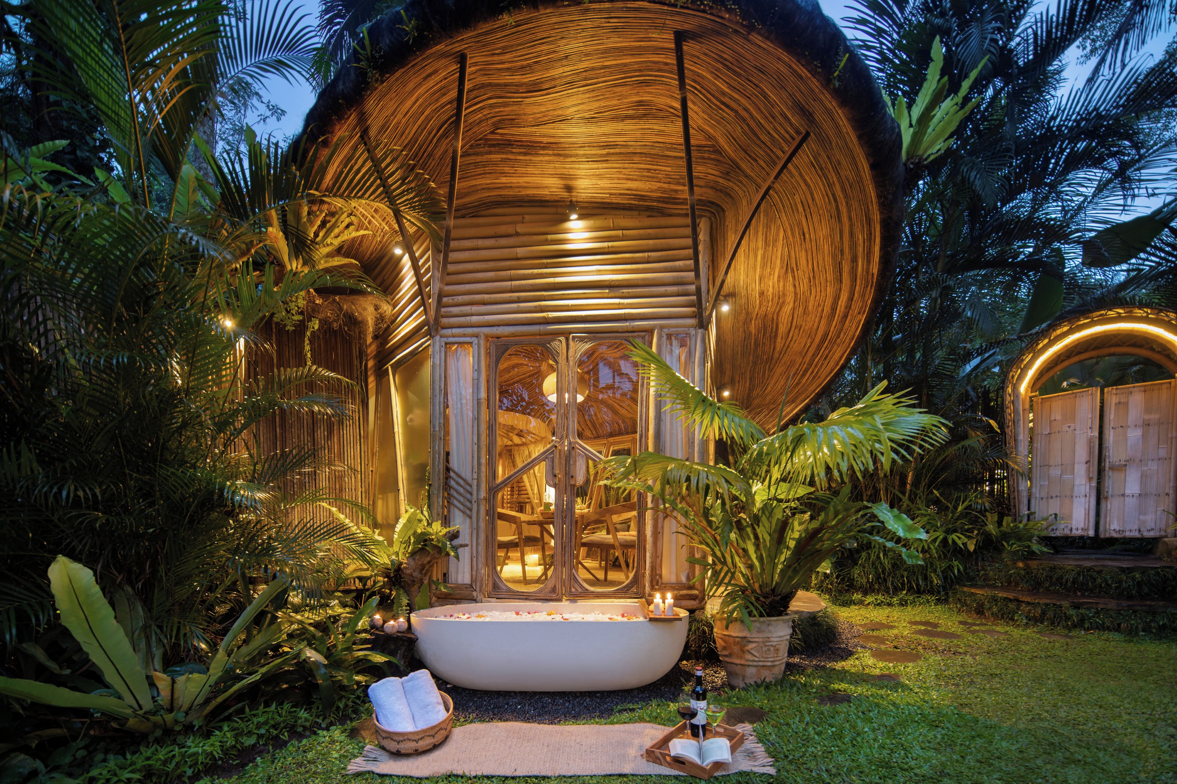 A circular wooden structure with a glass entrance, surrounded by tropical vegetation.