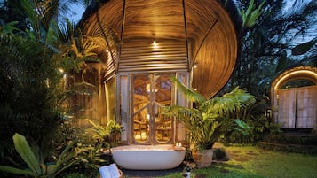 A circular wooden structure with a glass entrance, surrounded by tropical vegetation.