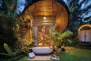 A circular wooden structure with a glass entrance, surrounded by tropical vegetation. - Hideout Eco Bamboo House Bali (Selat)