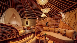A cozy, circular room with a thatched roof, a cushioned seating area, and a small table with a plant. - Hideout Eco Bamboo House Bali (Selat)
