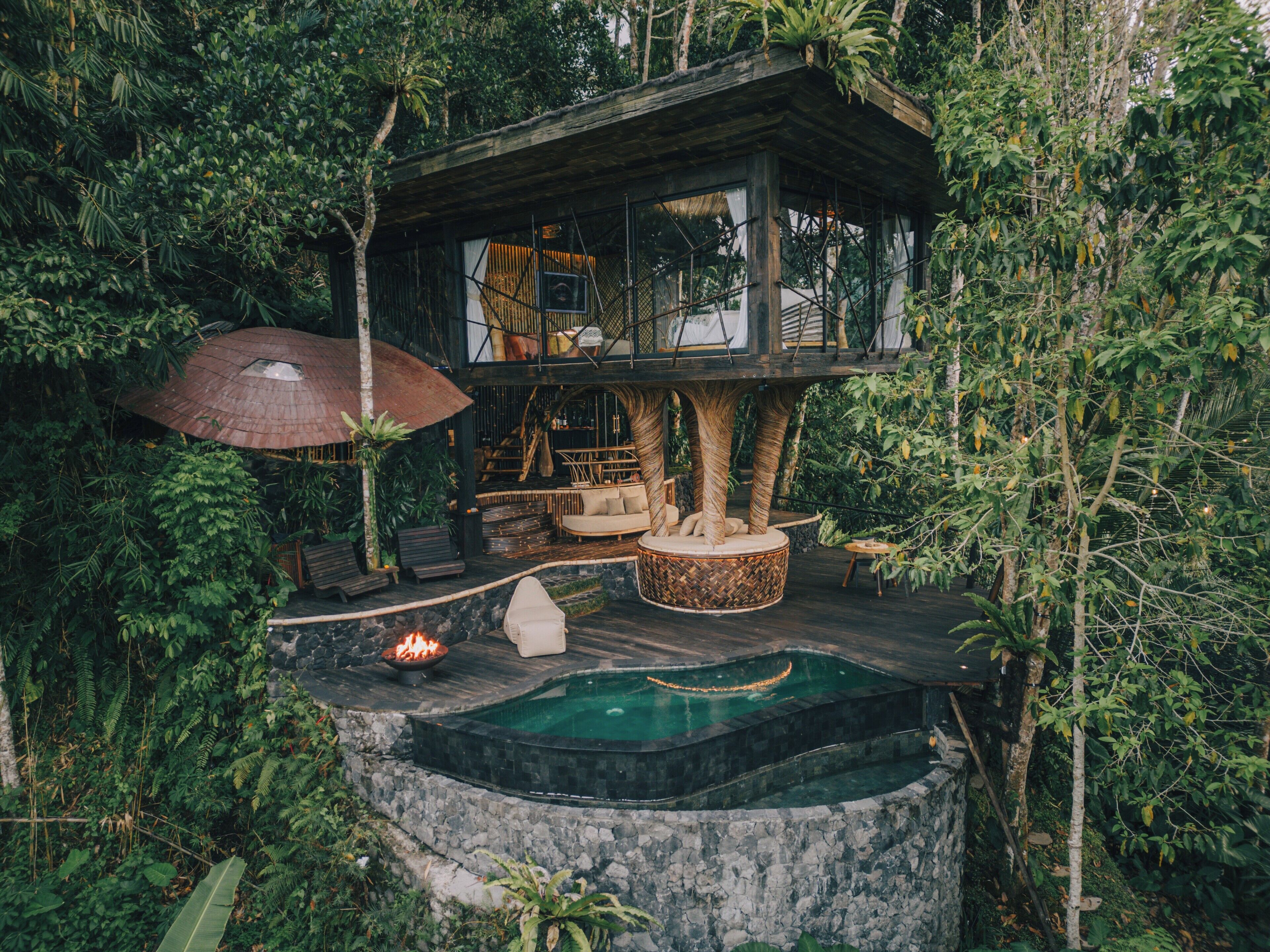 Una casa en un árbol con jacuzzi, zona de estar y techo de paja.