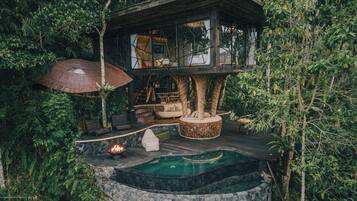 Una casa en un árbol con jacuzzi, zona de estar y techo de paja.
