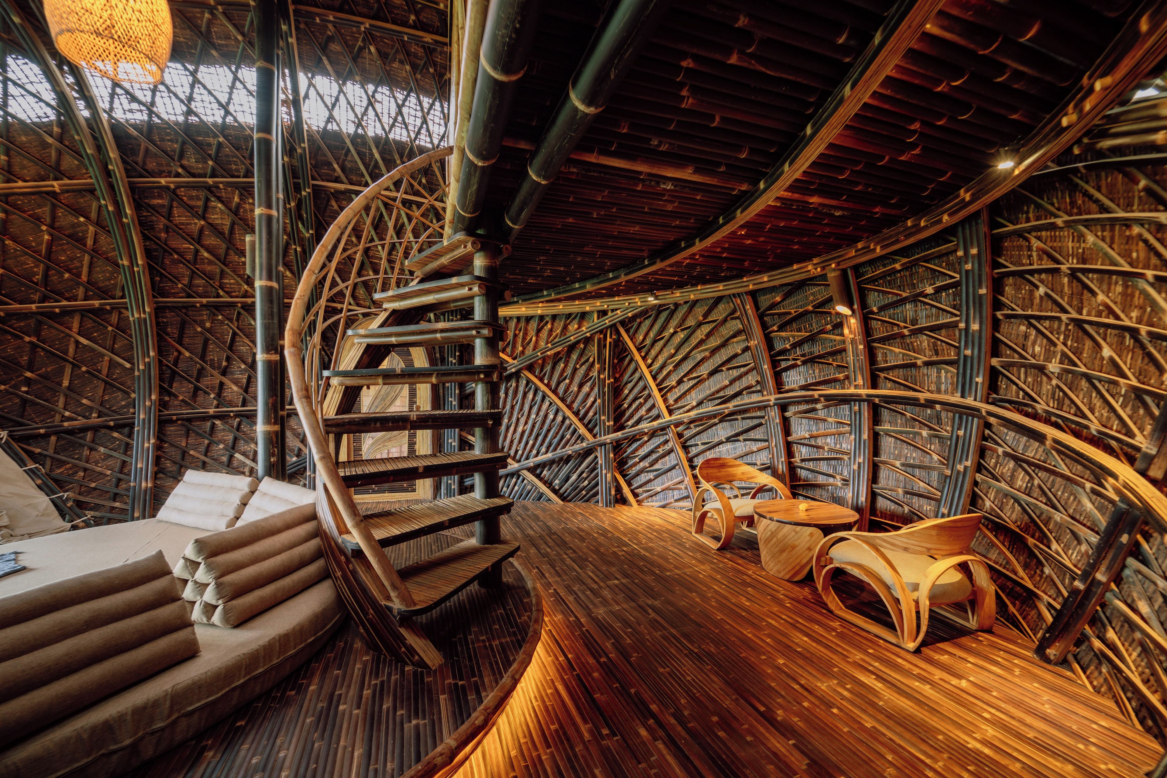 Una estructura circular de madera con escalera en espiral, zonas de estar y piso de madera.