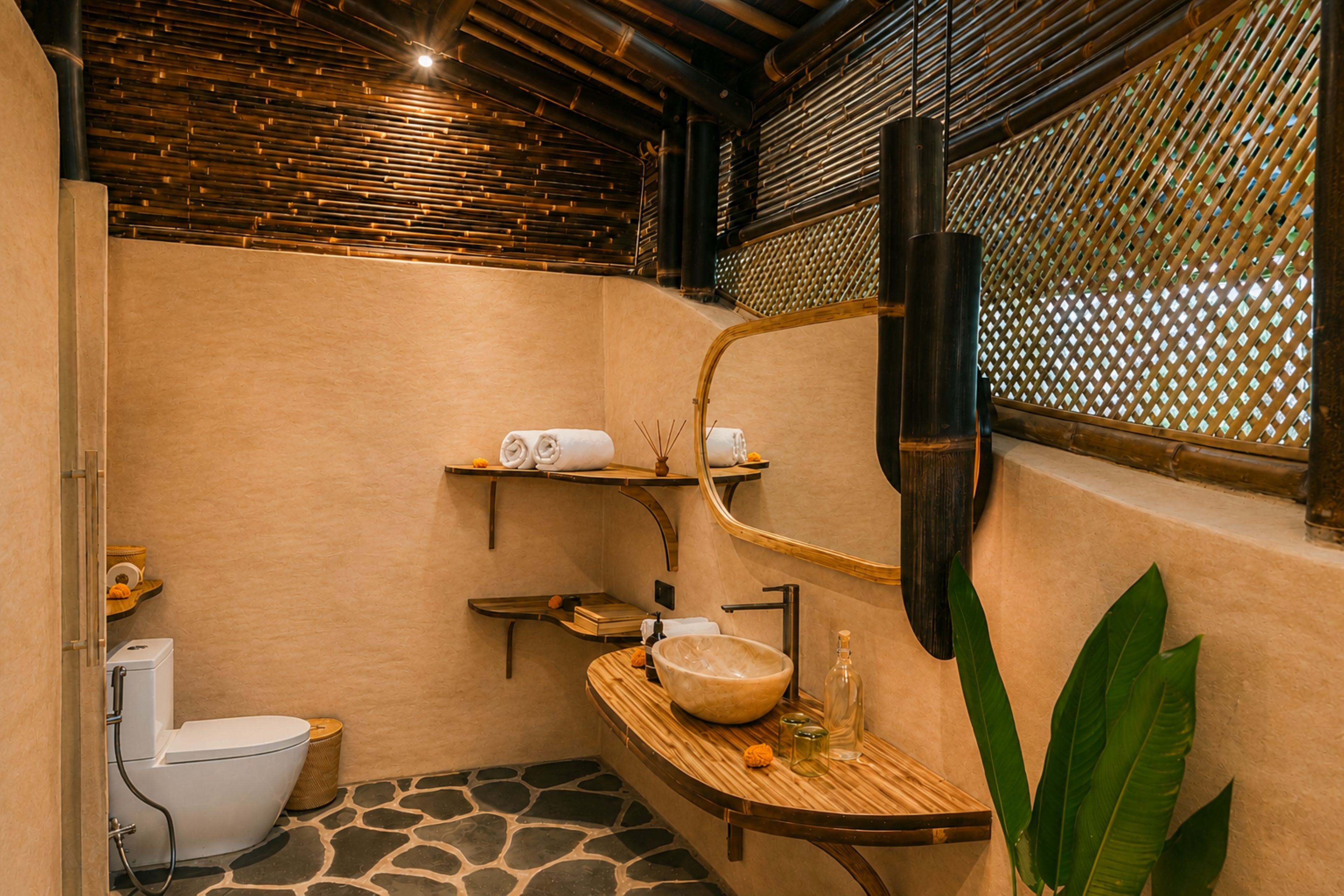 A bathroom with a stone floor, a white toilet, a wooden vanity with a bowl sink, and a large mirror.