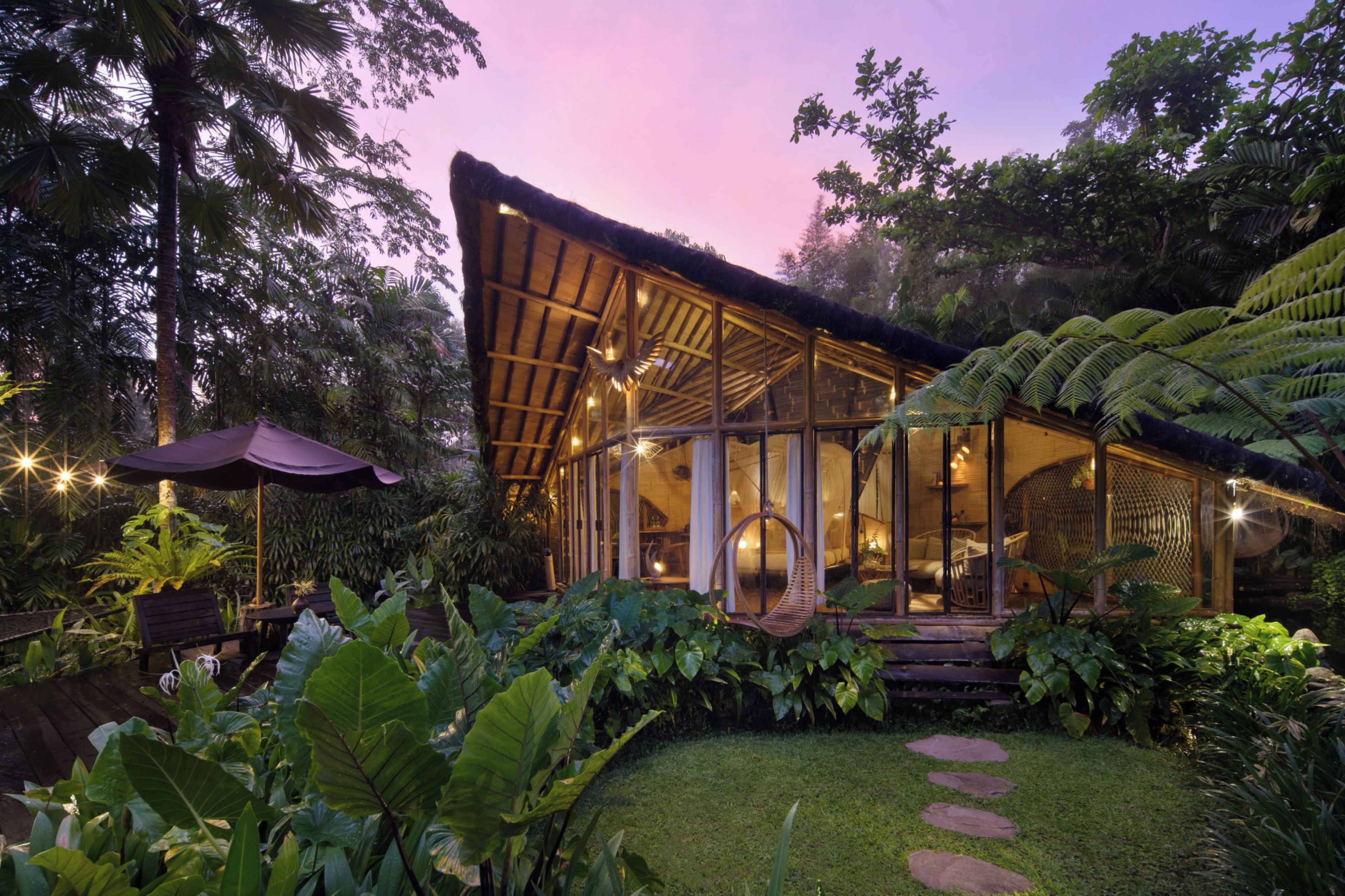 Una casa moderna con fachada de vidrio, rodeada de abundante vegetación y un jardín cuidado.