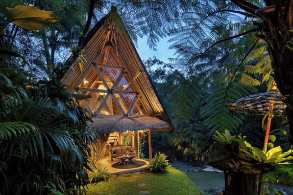 A thatched-roof hut with a central seating area, surrounded by lush greenery and a small water feature. - Hideout Eco Bamboo House Bali (Selat)
