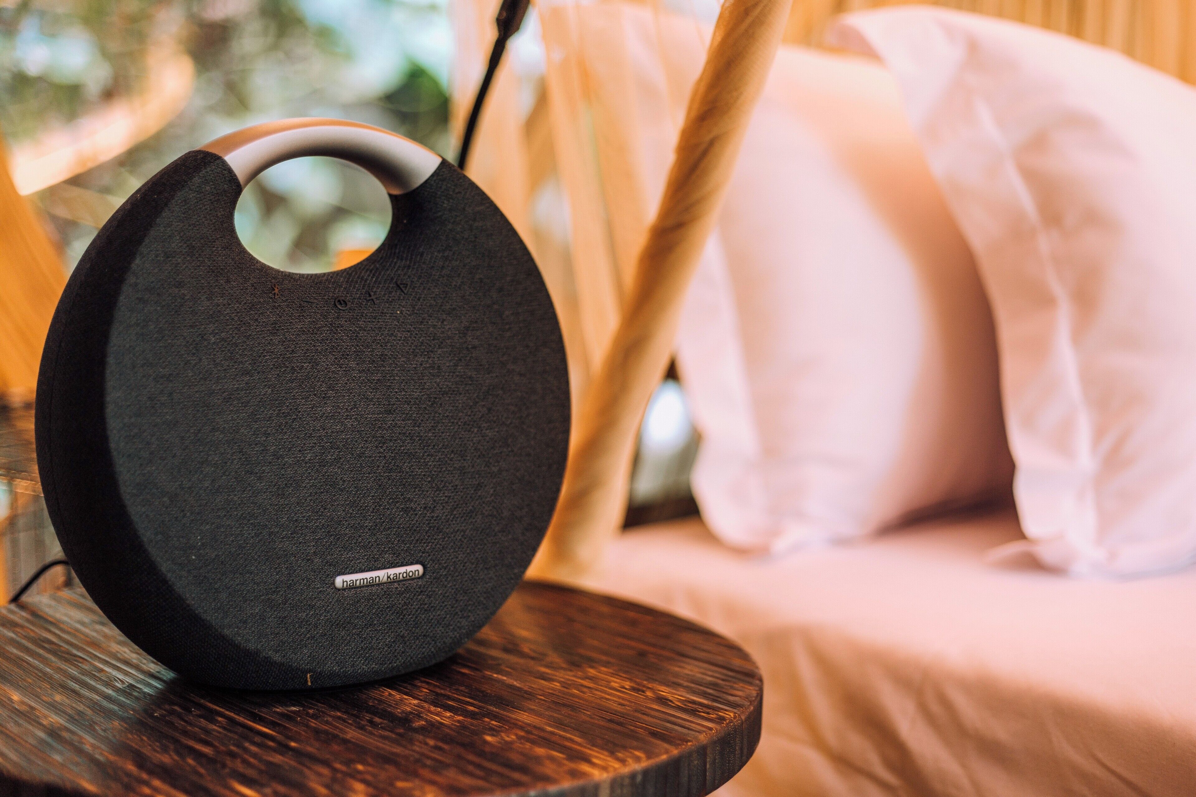 A black speaker with a circular cutout on a wooden table in a room with a bed and white pillows.