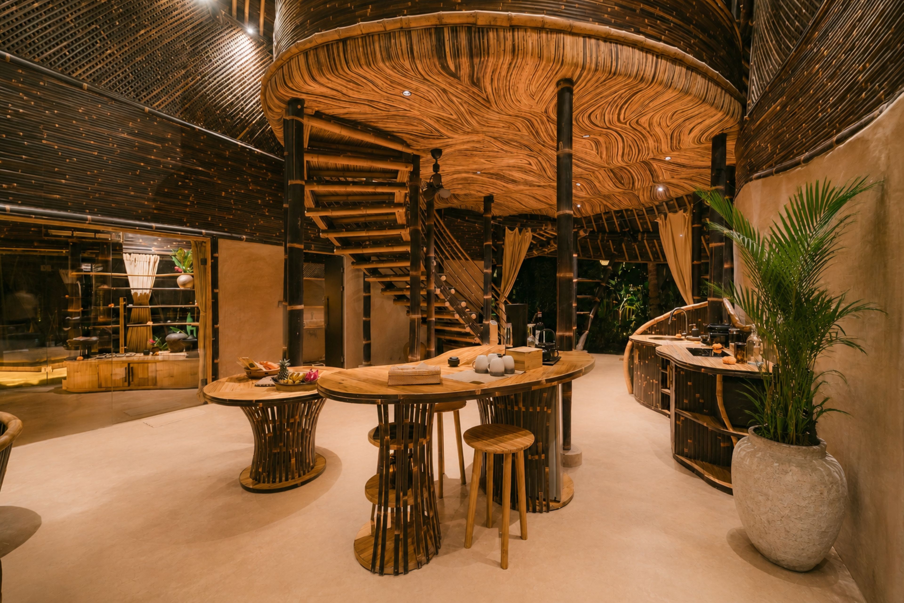 Un interior moderno con una mesa de madera central, taburetes y una planta grande en maceta.
