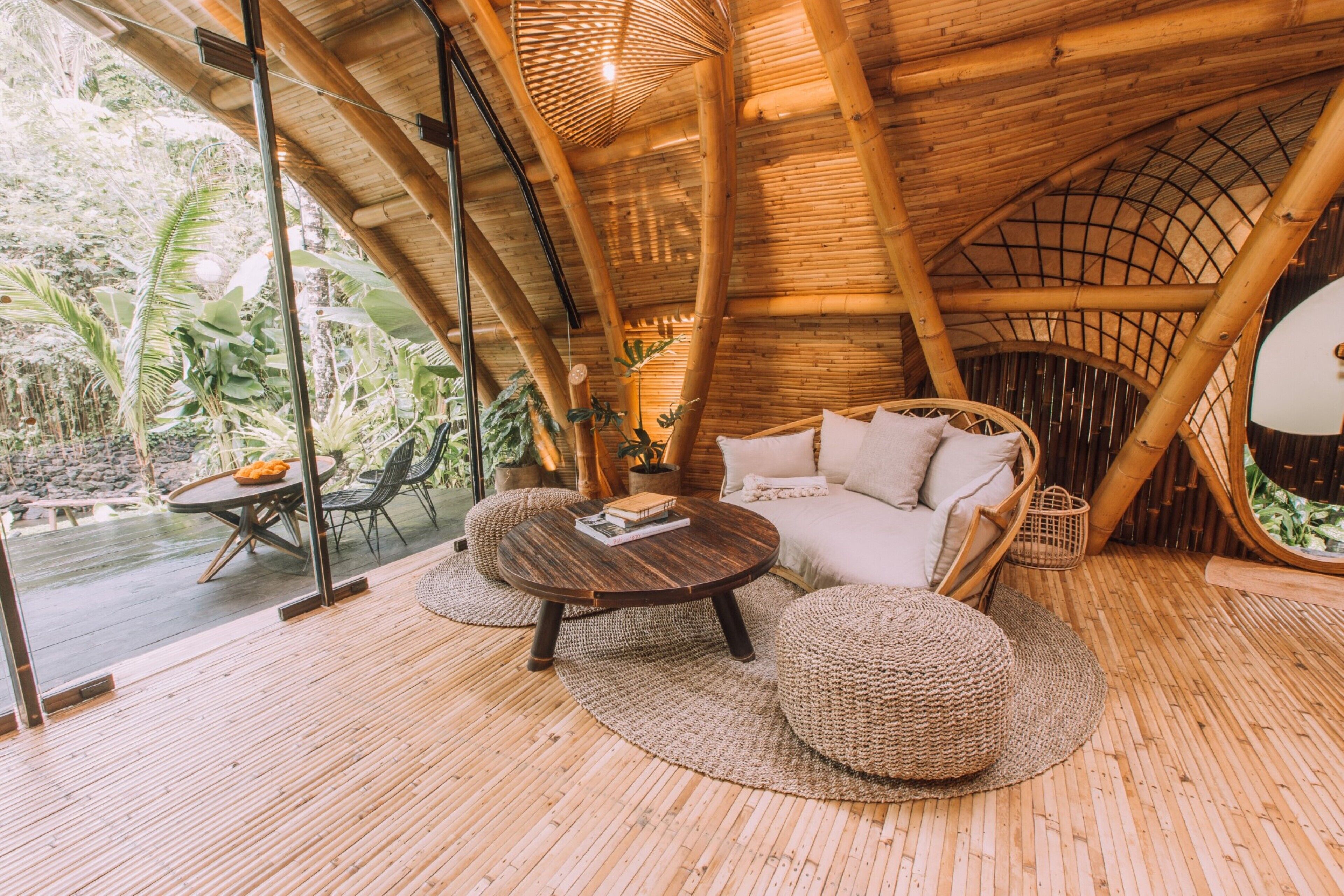 Un interior con motivos de bambú, una mesa redonda de madera, asientos acolchados y grandes ventanales con vistas al follaje circundante.