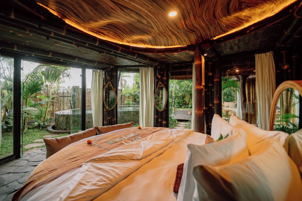 Une chambre spacieuse avec un grand lit, une vue sur le jardin et un plafond en bois original.