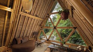 Un intérieur à thème bambou comprenant un lit, un coin salon et une vue sur l’extérieur.