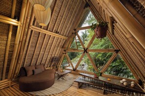 A bamboo-themed interior with a bed, seating area, and a view of the outdoors. - Hideout Eco Bamboo House Bali (Selat)
