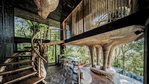 A spiral staircase leading to a wooden deck with a stone floor, surrounded by lush greenery. - Hideout Eco Bamboo House Bali (Selat)