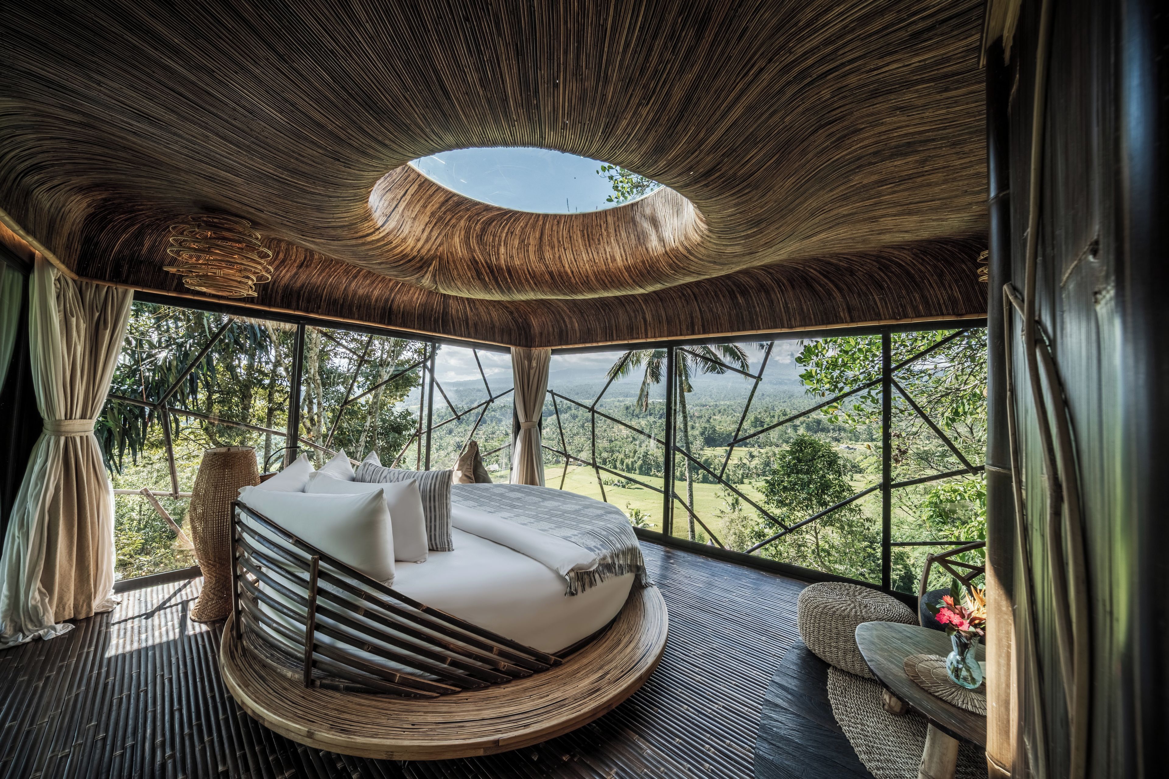 Una cama redonda con vistas a un paisaje boscoso a través de amplias ventanas.