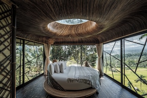 A bed in a room with a view of a forest and a unique ceiling design. - Hideout Eco Bamboo House Bali (Selat)