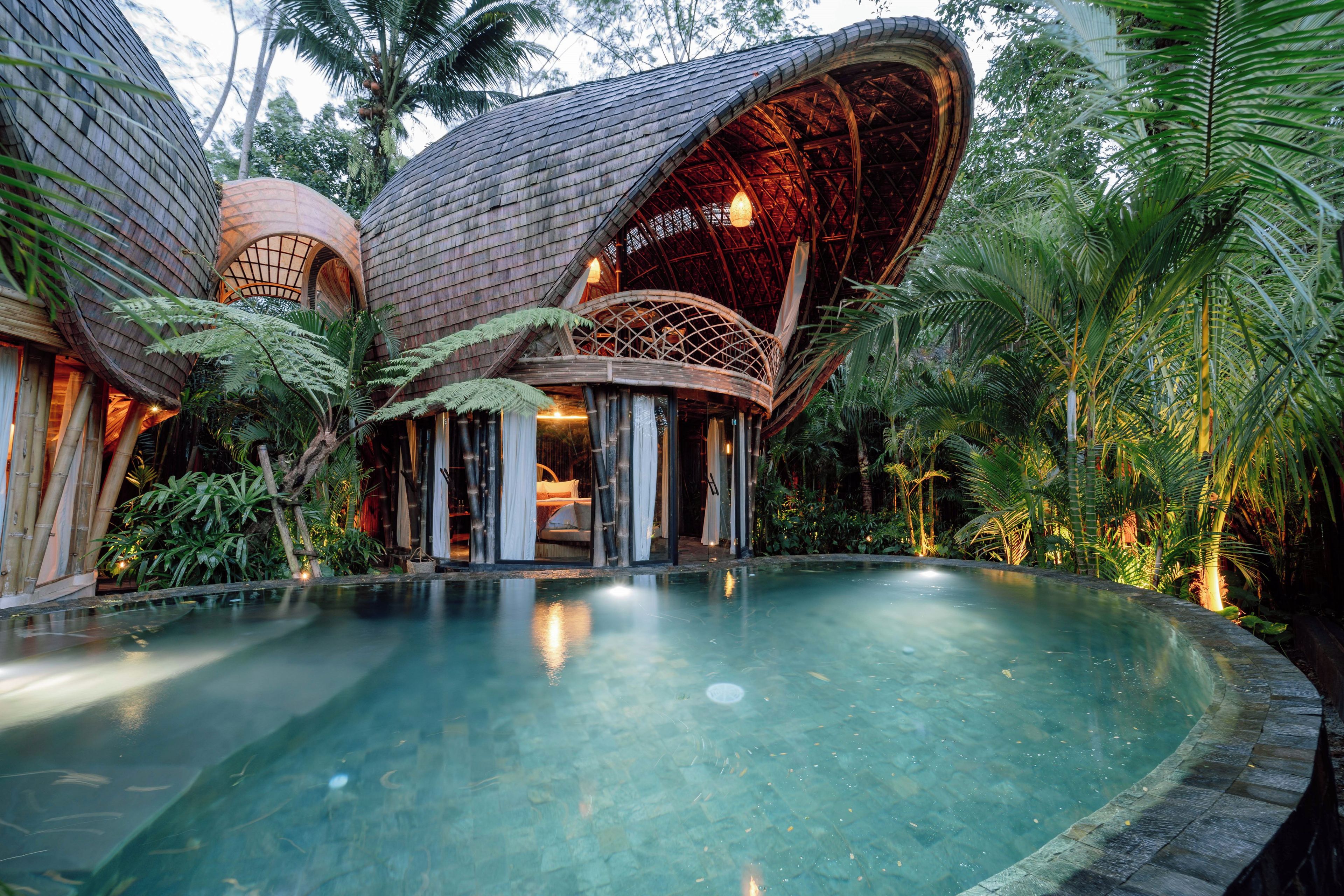 A resort with a large pool, a covered outdoor seating area, and lush tropical vegetation.