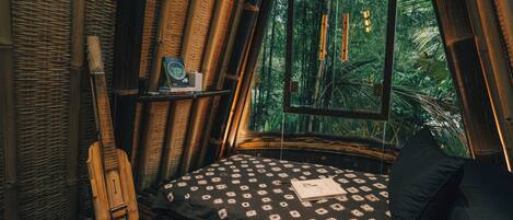 A room with a bed, a guitar, and a window overlooking a forest.