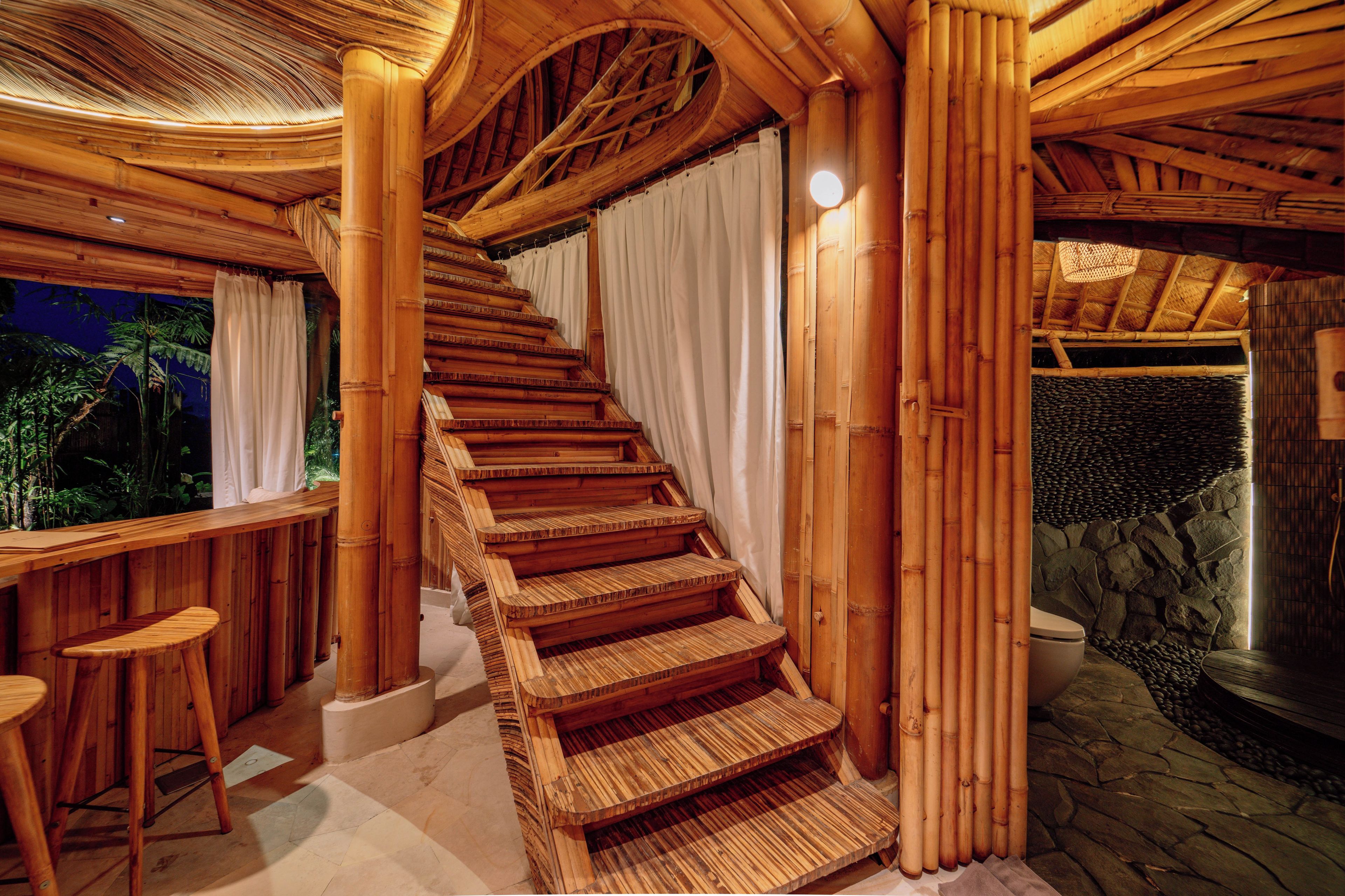 A wooden staircase with a curved design, leading to a room with a stone wall and a large water feature.