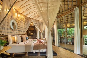 A spacious bedroom with a canopy bed, a large mirror, and a view of the outdoors. - Hideout Eco Bamboo House Bali (Selat)