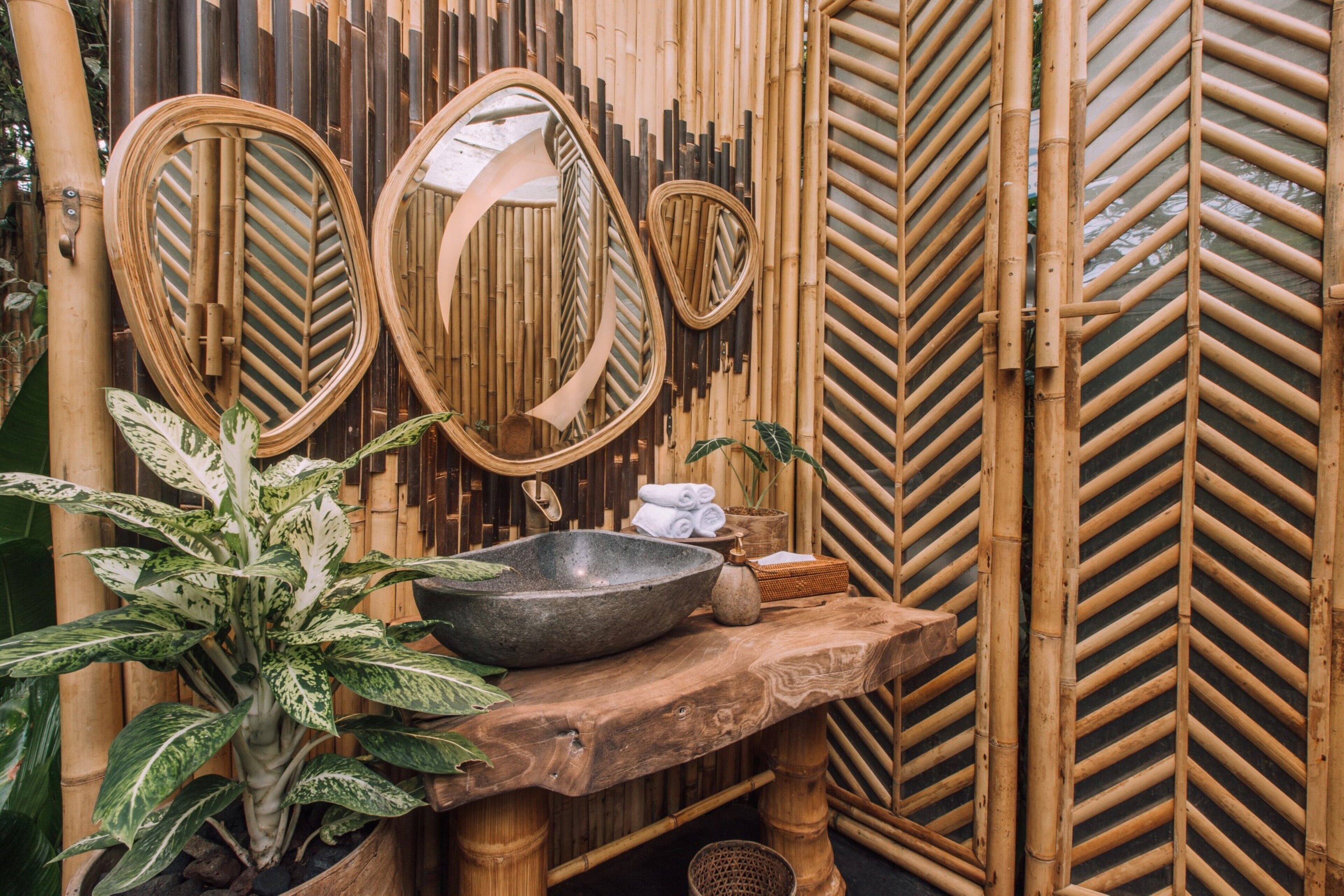 A bathroom with bamboo walls, a wooden sink, and two mirrors.