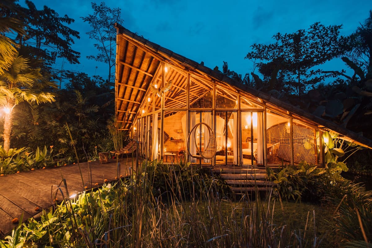 Un bâtiment doté d’un toit en verre et d’une façade en bois, entouré d’une végétation luxuriante.