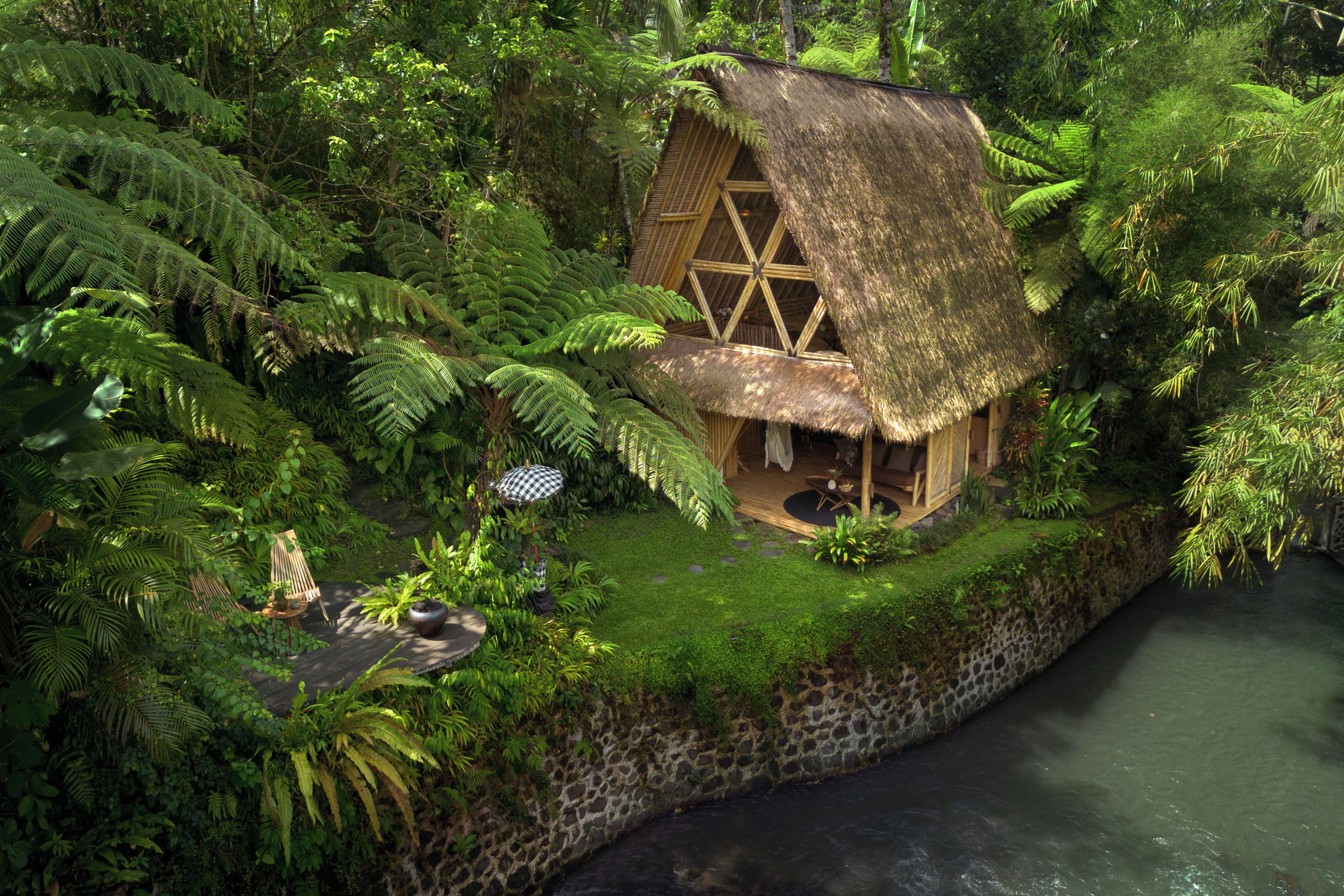 Une maison à toit de chaume, entourée d’une végétation luxuriante et d’un mur de pierre.