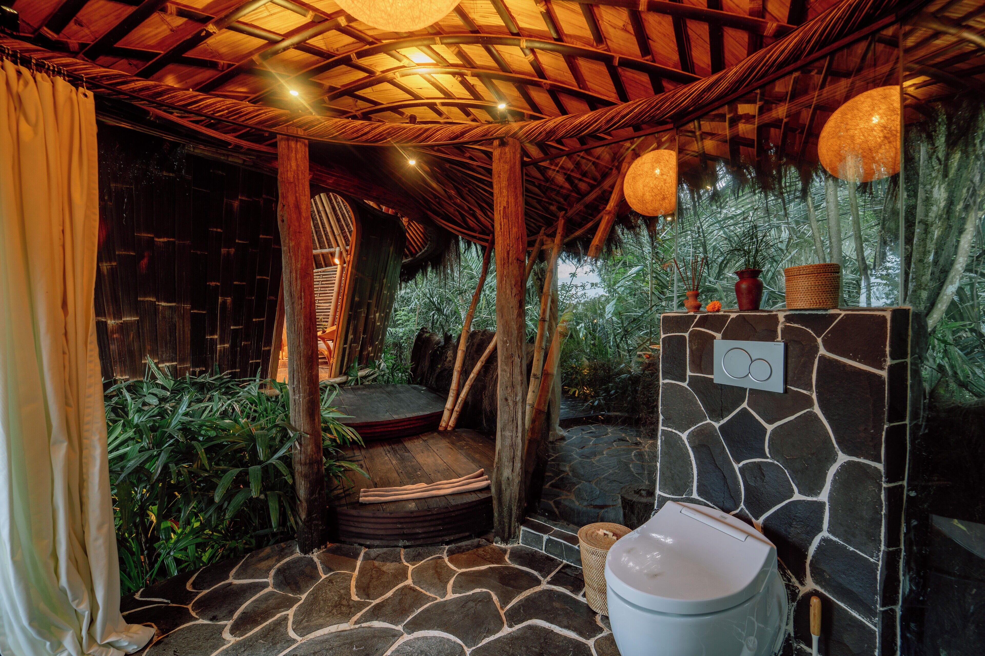 Un bagno rustico con pavimento in pietra, una panca di legno, un water e un muro in pietra con un cesto di vimini.