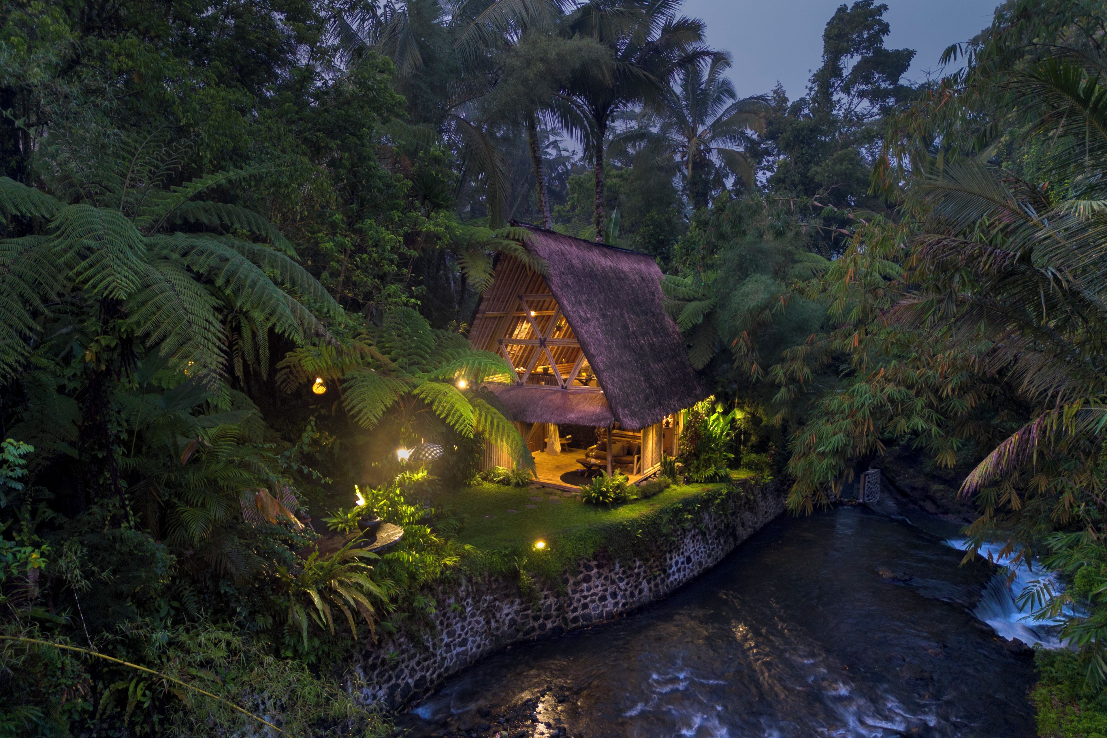Ein Haus mit einem Strohdach, umgeben von üppiger tropischer Vegetation und einem plätschernden Bach.