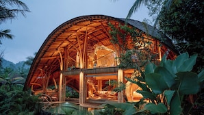 A large, open-air structure with a curved roof, surrounded by lush tropical vegetation. - Hideout Eco Bamboo House Bali (Selat)